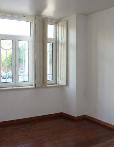 A bright, empty room with white walls, three tall windows letting in natural light, and a polished wooden floor.