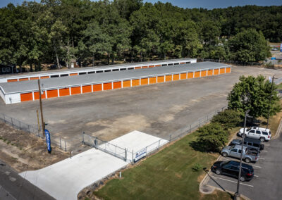 Aerial view of a self-storage facility with orange doors, a paved entrance, and an adjacent parking lot.