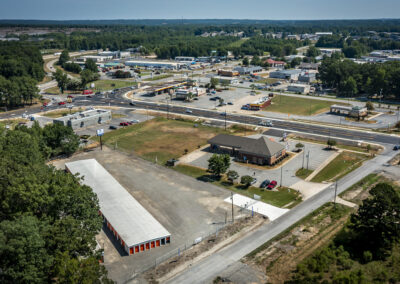 Aerial view of a self-storage facility with several commercial buildings, a gas station, and roads in a suburban area.