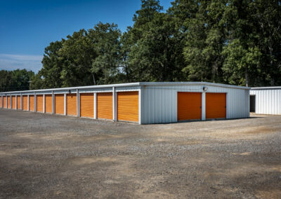 Long rows of metal self-storage units with orange roll-up doors in a gravel lot.
