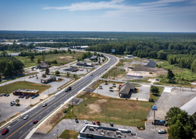 Aerial view of a highway running through a commercial area with restaurants and parking lots surrounded by dense forest.